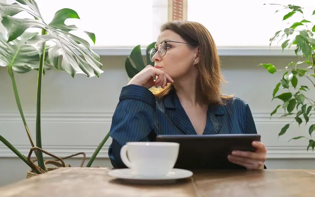 Eine Frau im Businessanzug sieht nicht glücklich aus. In der Hand hält sie ein Tablet, schaut aber traurig zur Seite. Vor ihr auf dem Tisch steht eine Tasse mit Tee.